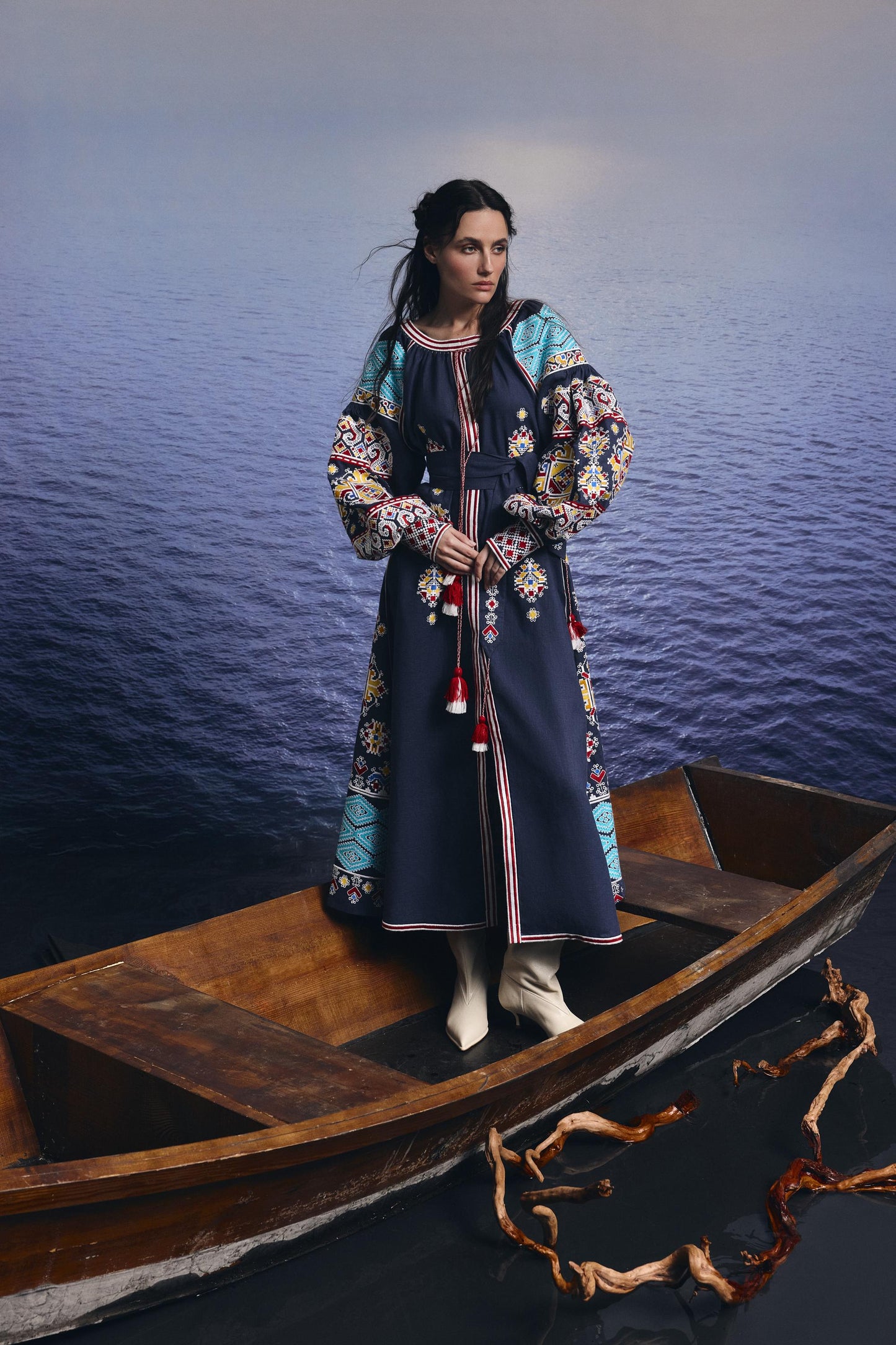 Blue embroidered linen wedding dress in Ukrainian vyshyvanka style, boho Mexicana design, modeled on a wooden boat.