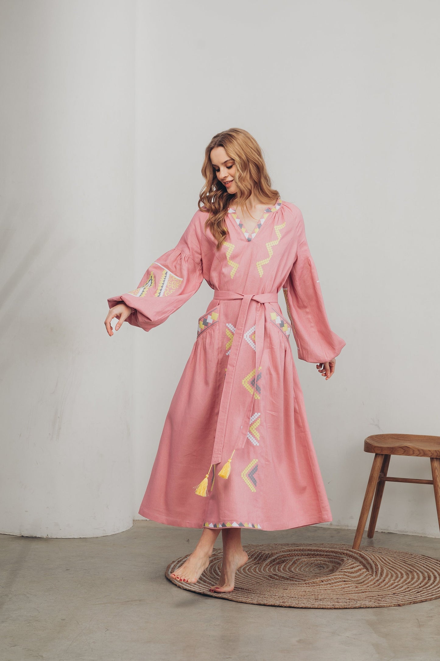 Woman wearing a pink linen embroidered Vyshyvanka dress with belt, in boho Ukrainian folk style, featuring pockets.