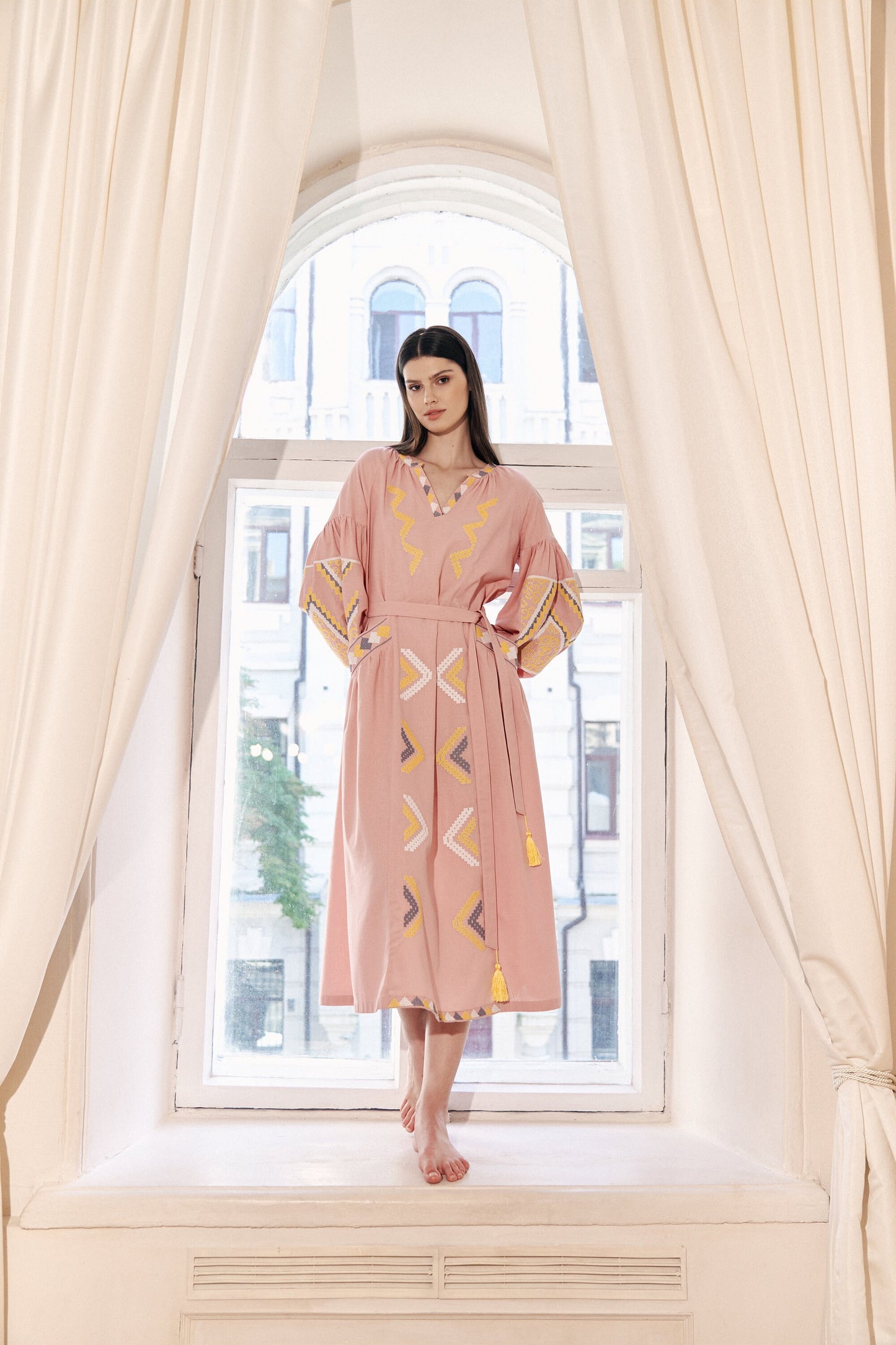 Woman wearing pink linen embroidered Vyshyvanka dress with pockets and belt, showcasing Ukrainian boho folk style.