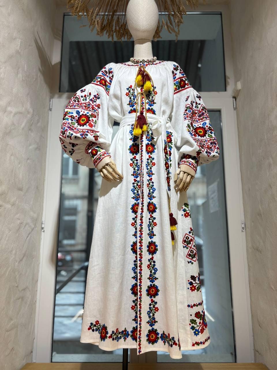 White linen embroidered wedding dress with Ukrainian folk motifs and boho style, featuring detailed red and black floral designs on sleeves and bodice.
