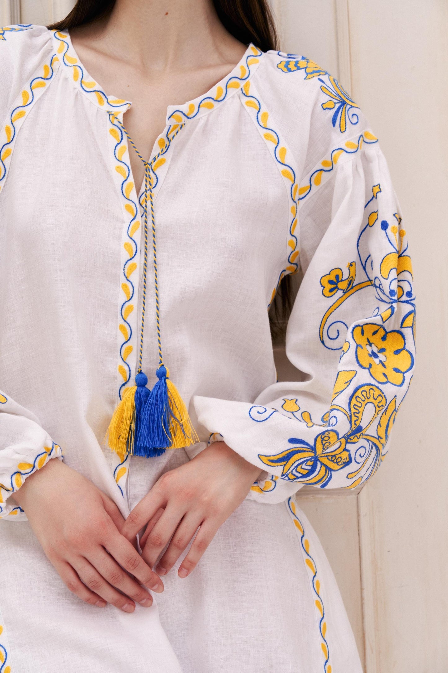 White linen embroidered wedding dress with blue and yellow Ukrainian Vyshyvanka boho style floral patterns and tassels.
