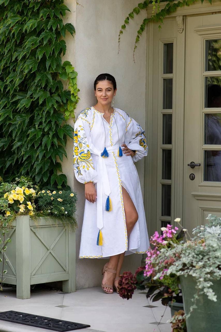 Woman wearing a white linen embroidered Ukrainian vyshyvanka wedding dress with boho style, standing by a garden door.