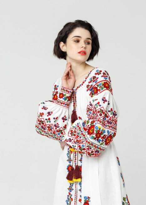Woman wearing a Ukrainian vyshyvanka white linen dress with colorful embroidery in boho style.