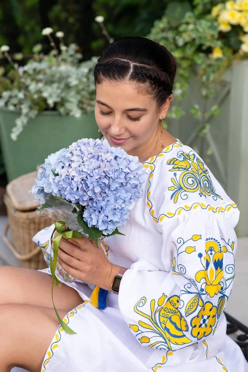 Woman in embroidered dress holding a bouquet of hydrangeas, showcasing Ukrainian folk art style.
