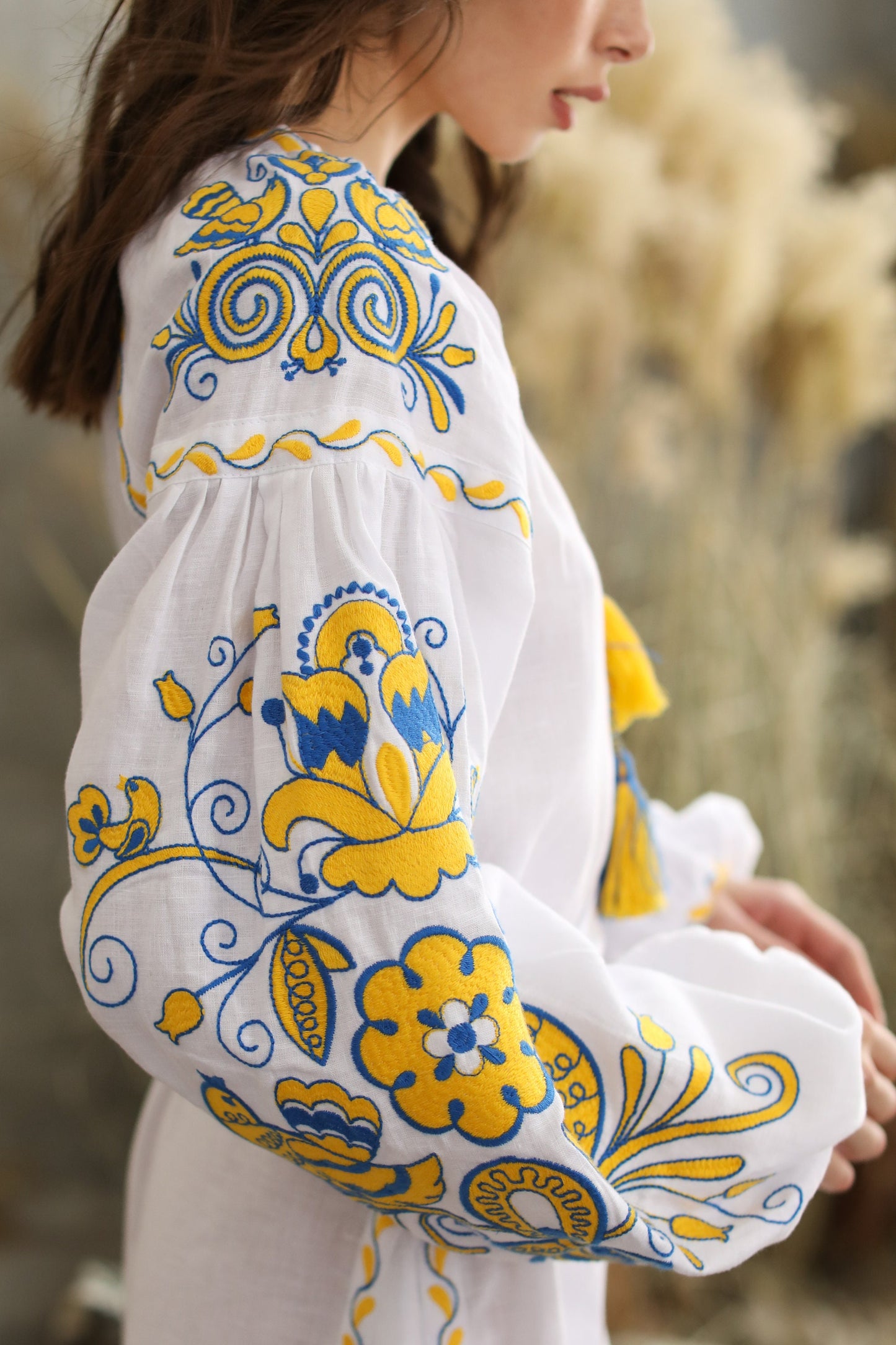 White linen wedding dress with vibrant blue and yellow Ukrainian embroidery, featuring intricate patterns symbolizing the Tree of Life.