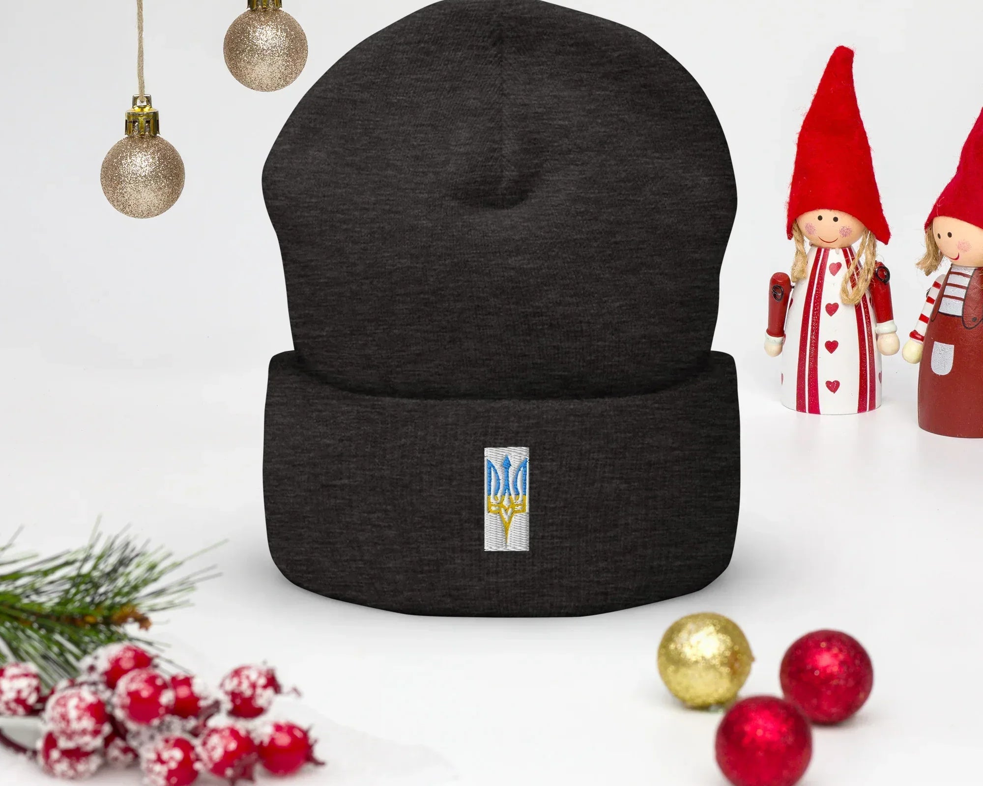 Black beanie with embroidered Ukrainian Trizub symbol displayed on festive background with Christmas decorations.