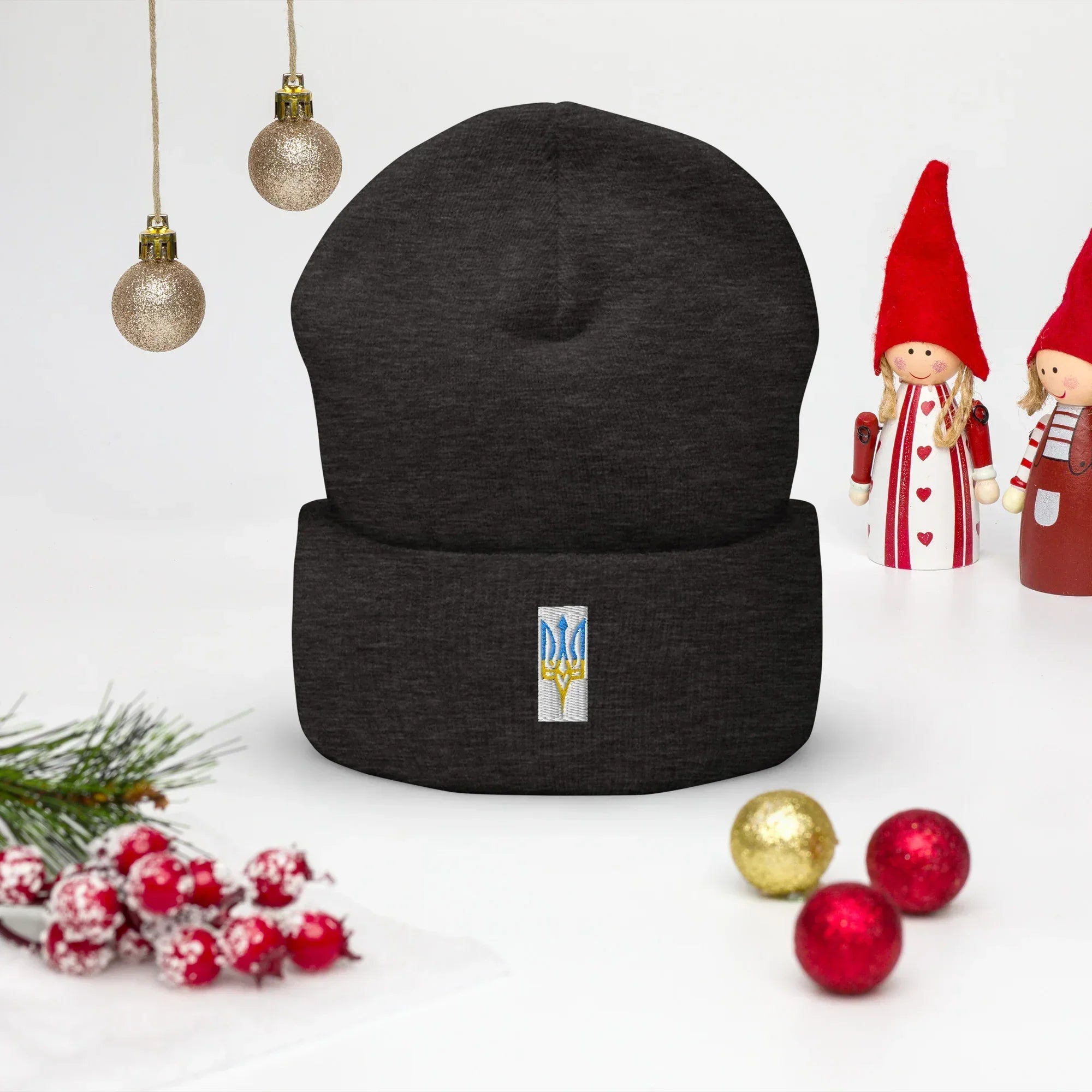 Black beanie with embroidered Ukrainian Trizub symbol displayed on festive background with Christmas decorations.