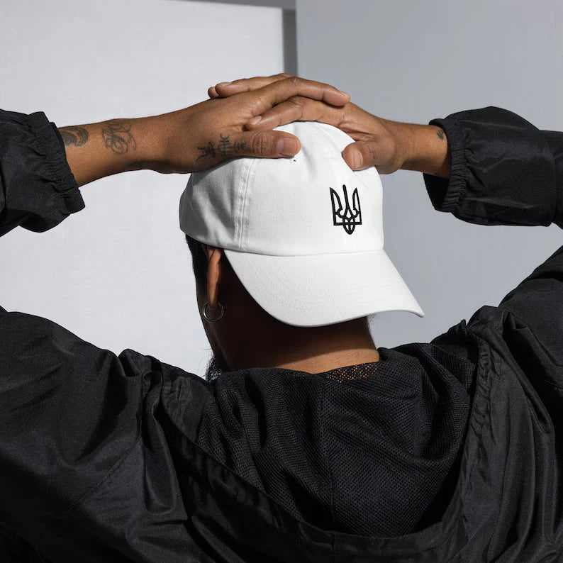 Black winter hat with embroidered trident symbol, surrounded by festive decorations and Christmas ornaments.
