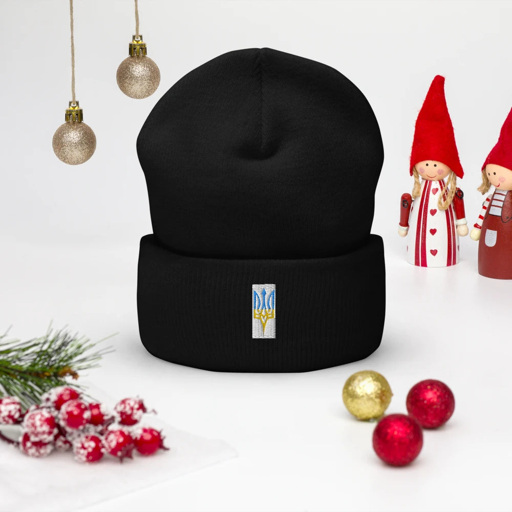 Black winter hat with embroidered trident symbol, surrounded by festive decorations and Christmas ornaments.