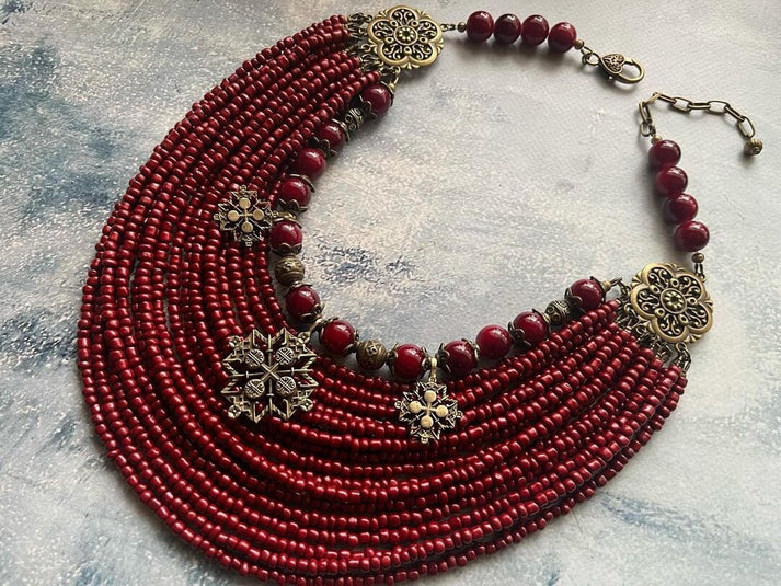 Handcrafted red beaded necklace with antique gold floral accents and adjustable clasp, laid on textured background.