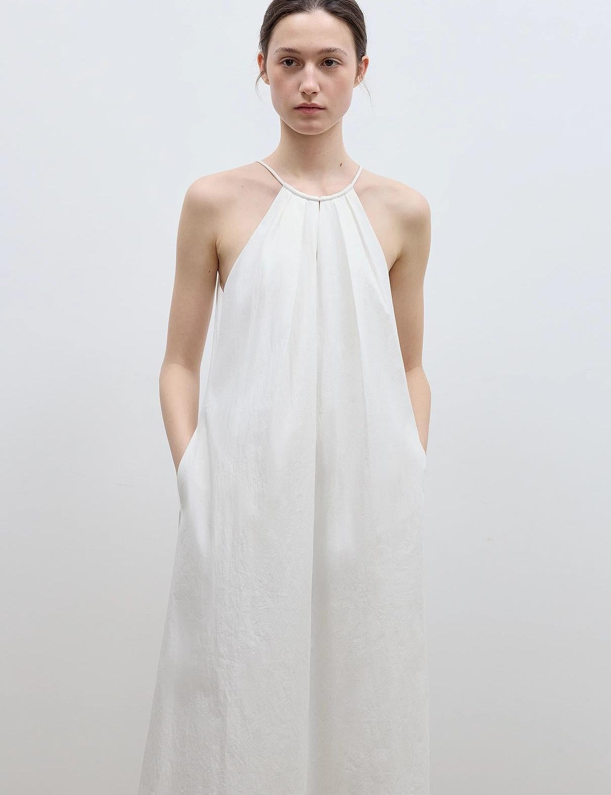 Woman wearing Veridia Halter‑Pleat Maxi Dress in white, featuring a cotton-rope halter and V-shaped front cut-out with pleated neckline.