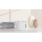 White enamel mug 12oz with silver rim on a table, ideal for outdoor adventures and custom designs.