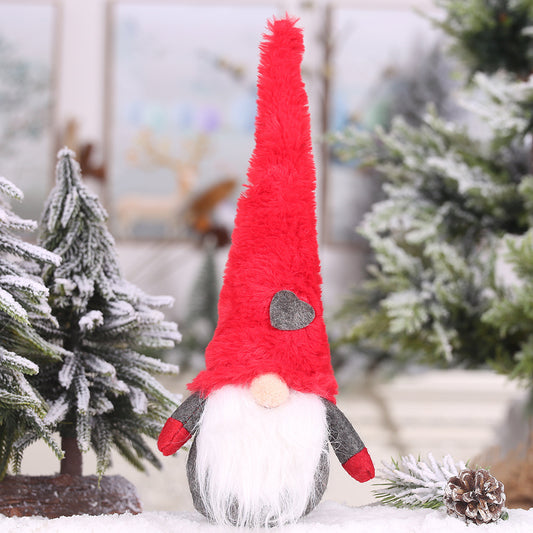 Plush Christmas decoration forest man doll with long red hat amidst snowy trees, adding whimsical charm to holiday décor.