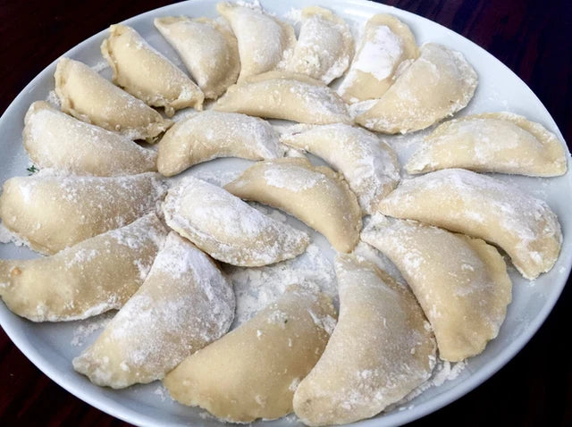 Homemade frozen Ukrainian varenyky dumplings on a plate with potato, cabbage, or farmer's cheese fillings, dusted in flour.