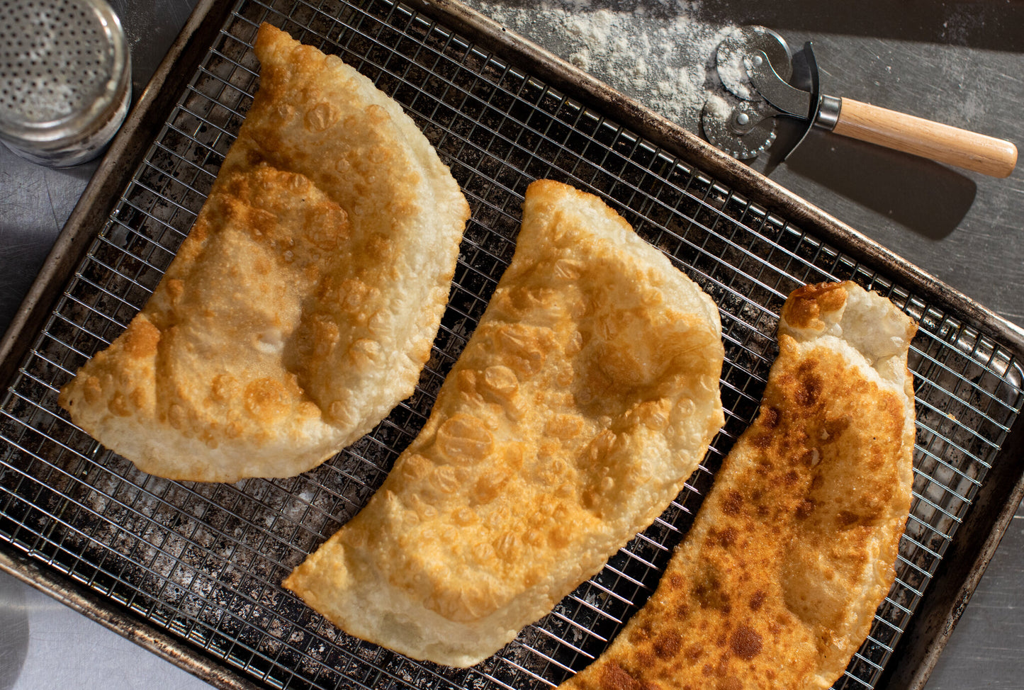 Three crispy homemade Ukrainian chebureki pastries on a wire rack with a golden-brown crust.