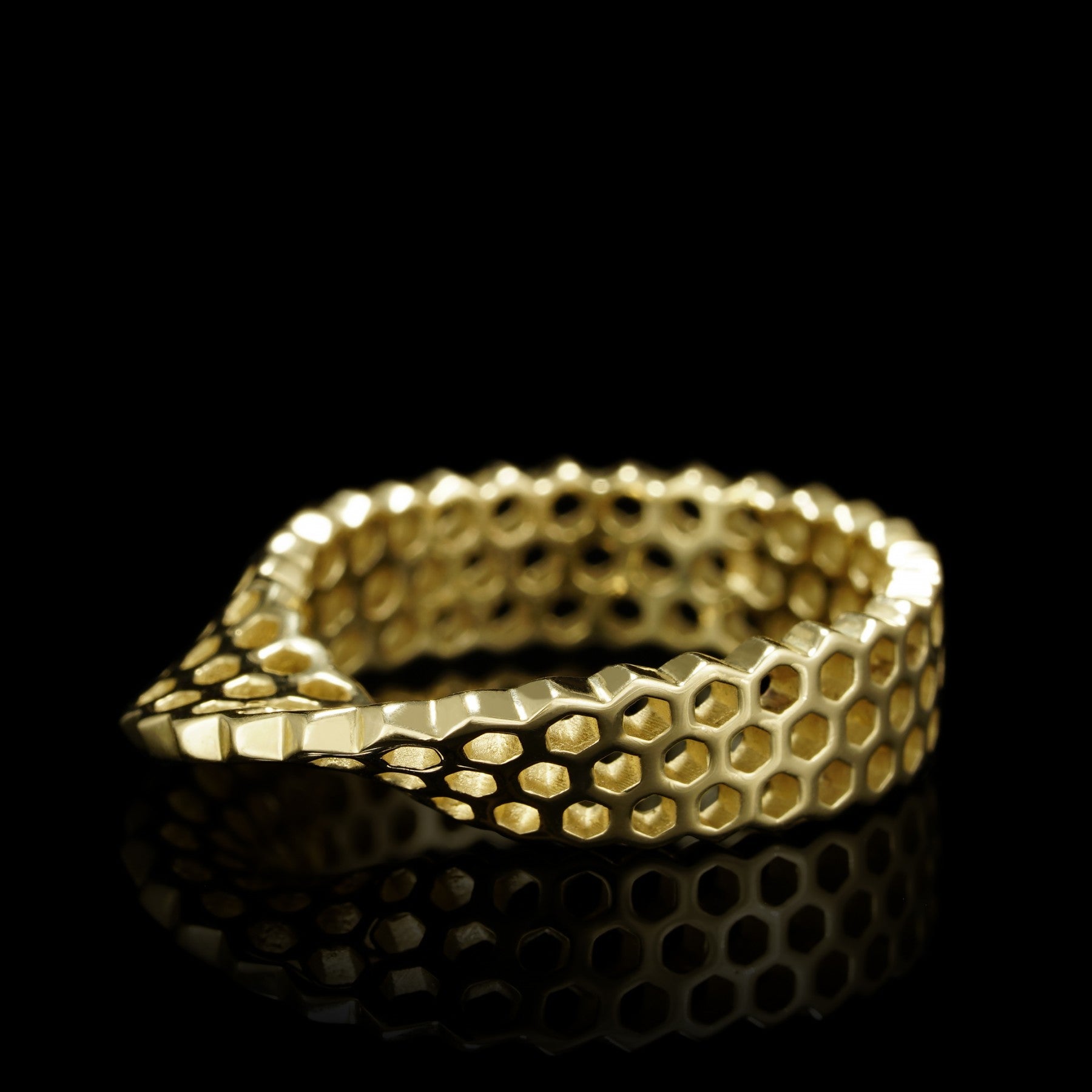 14K yellow gold honeycomb textured ring against a black background, showcasing its unique design and luxurious glow.