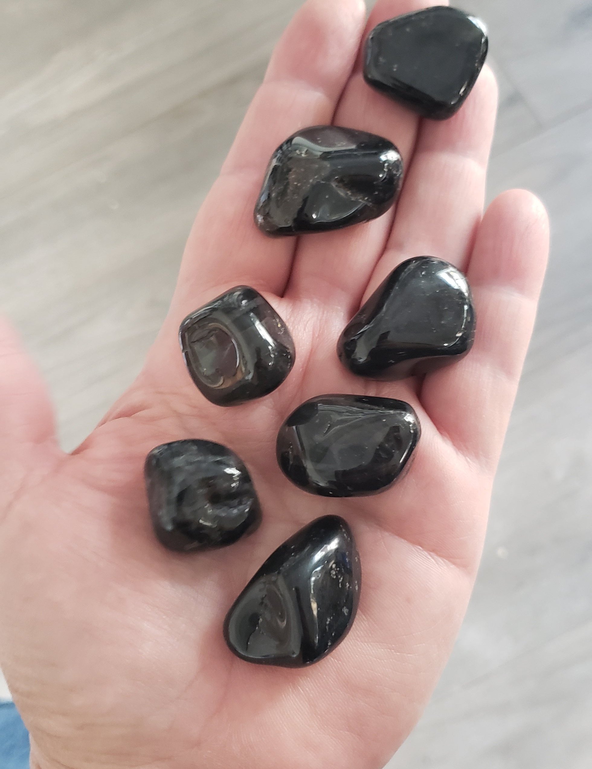 Hand holding Nyra black onyx tumbled stones, offering grounding and spiritual protection.