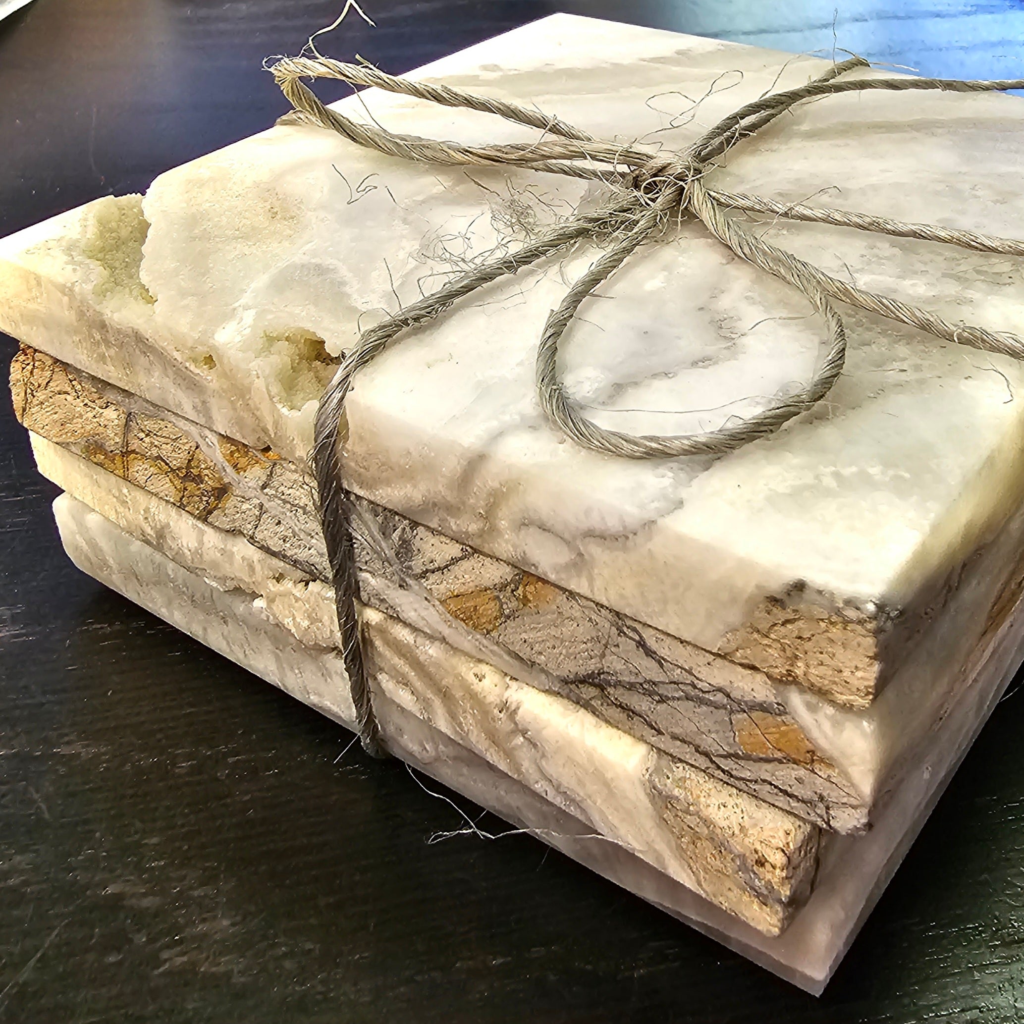 Calvera handcrafted onyx coaster set of four tied with twine, showcasing unique veining and color variations on a dark table.