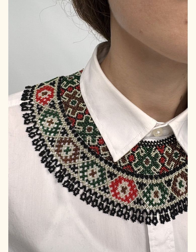Ukrainian Kryza necklace in green, red, and beige, handmade with intricate folk patterns, worn over a white shirt collar.
