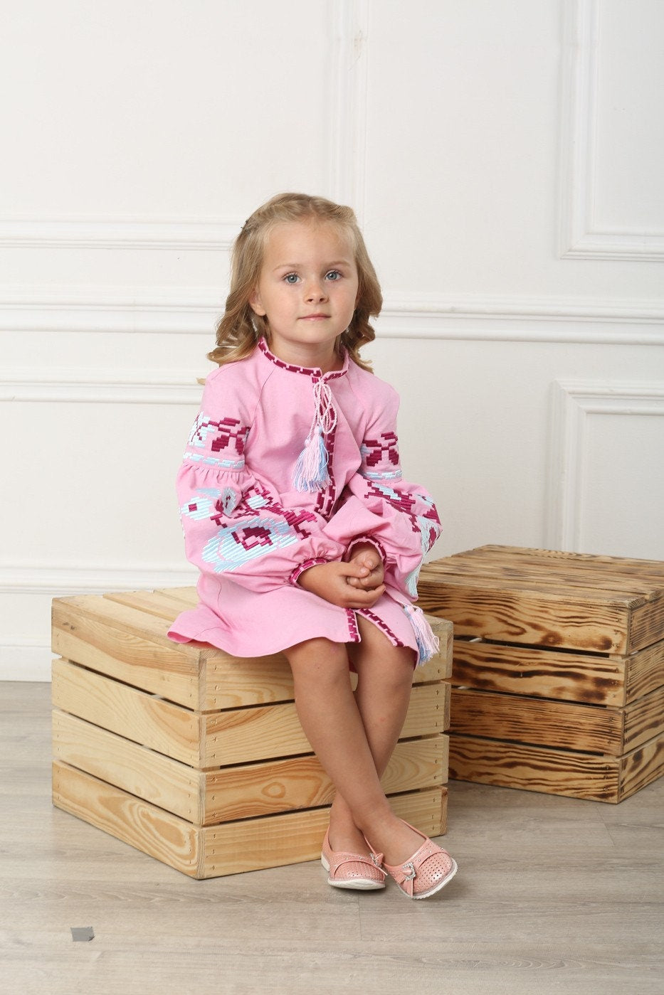 Young girl wearing a pink embroidered linen dress with floral cross-stitch, showcasing Ukrainian vyshyvanka style.