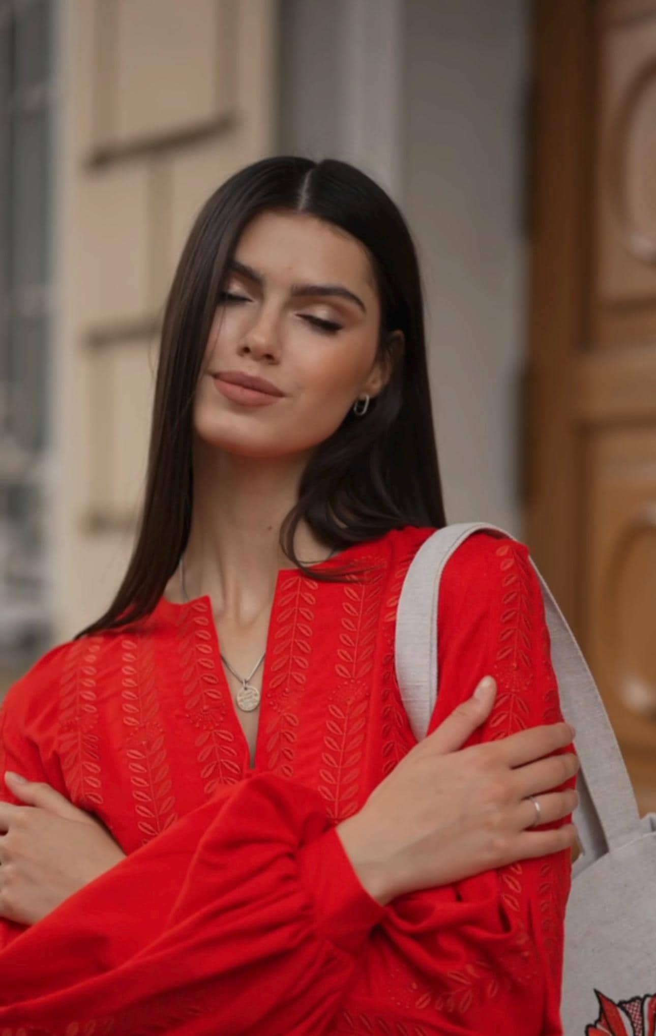 Woman wearing red linen embroidered blouse in Ukrainian vyshyvanka style, arms crossed, outdoors, showcasing boho fashion.