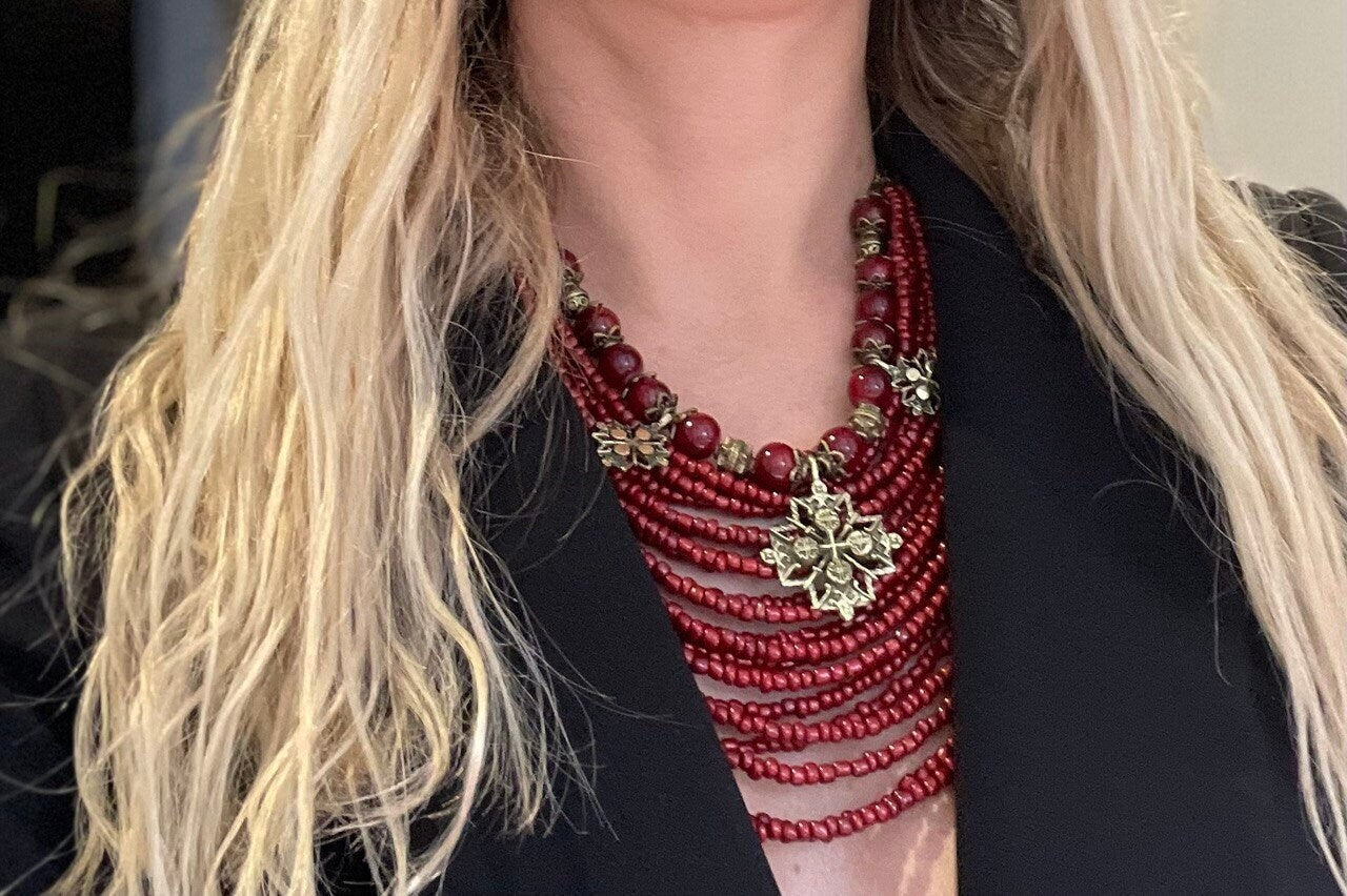 Close-up of red Ukrainian necklace with glass beads and bronze charms, worn on black outfit, ideal ethnic jewelry gift for her.
