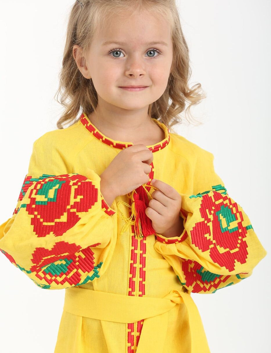 Girl in yellow linen embroidered dress with Ukrainian floral cross-stitch, smiling, traditional vyshyvanka style, festive clothing.