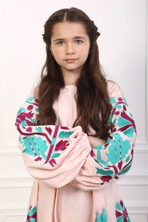 Girl wearing a 2025 pink linen embroidered dress with Ukrainian boho vyshyvanka design and belt, featuring long gathered sleeves.