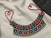 Handmade Ukrainian Sylyanka necklace with colorful Czech seed beads featuring geometric and floral patterns on a fabric backdrop.