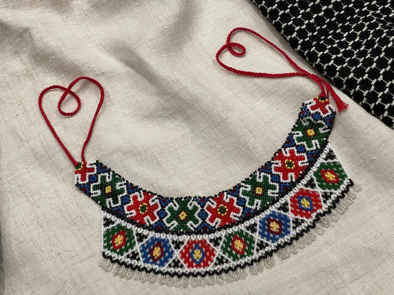 Handmade Ukrainian Sylyanka necklace with colorful Czech seed beads featuring geometric and floral patterns on a fabric backdrop.