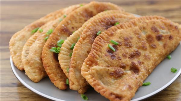 Plate of homemade Ukrainian chebureki pastries, crispy and golden brown, filled with juicy beef and garnished with green onions.