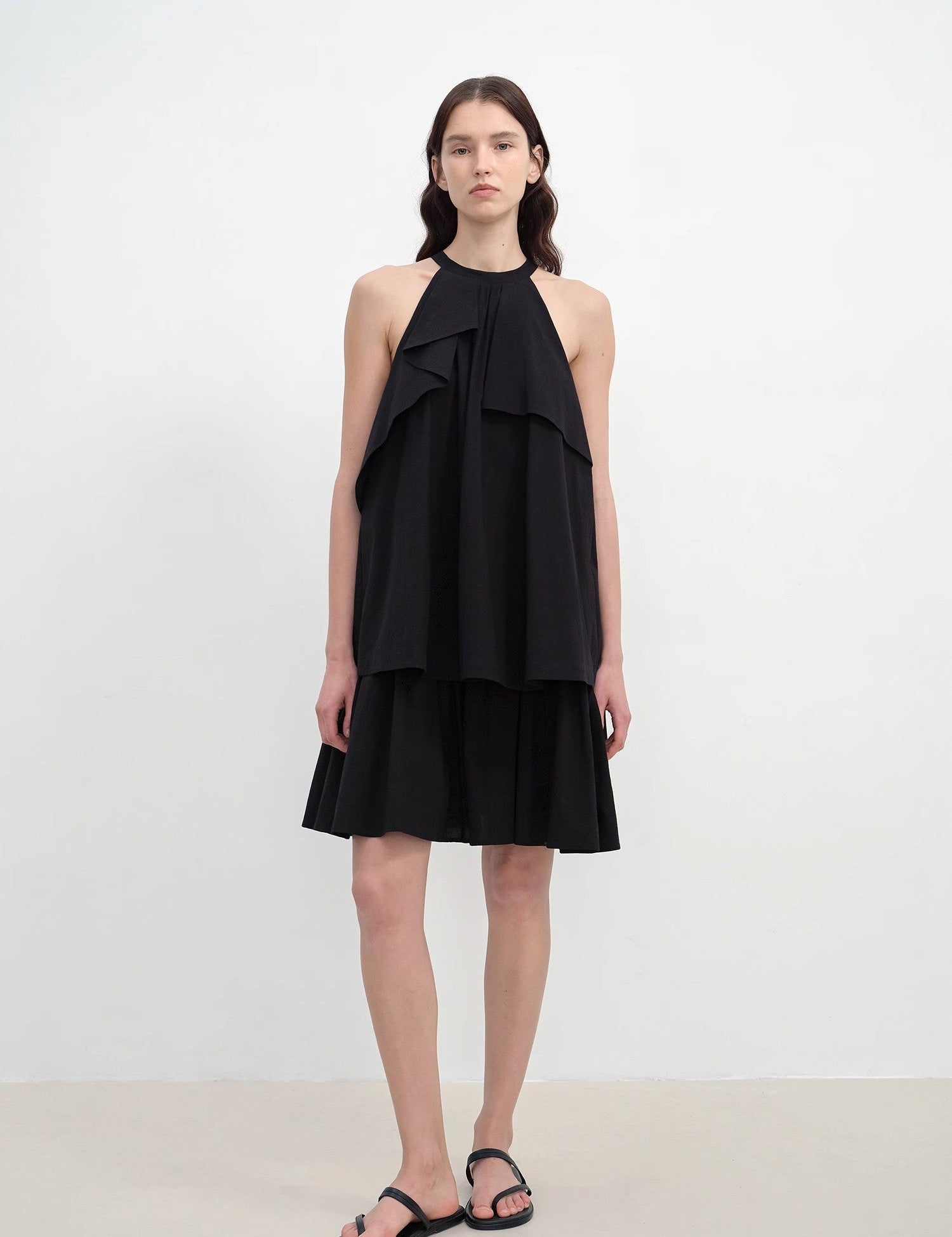 Model wearing Islanda Textured Cotton Halter Dress in black with asymmetric pleated neckline and A-line silhouette.