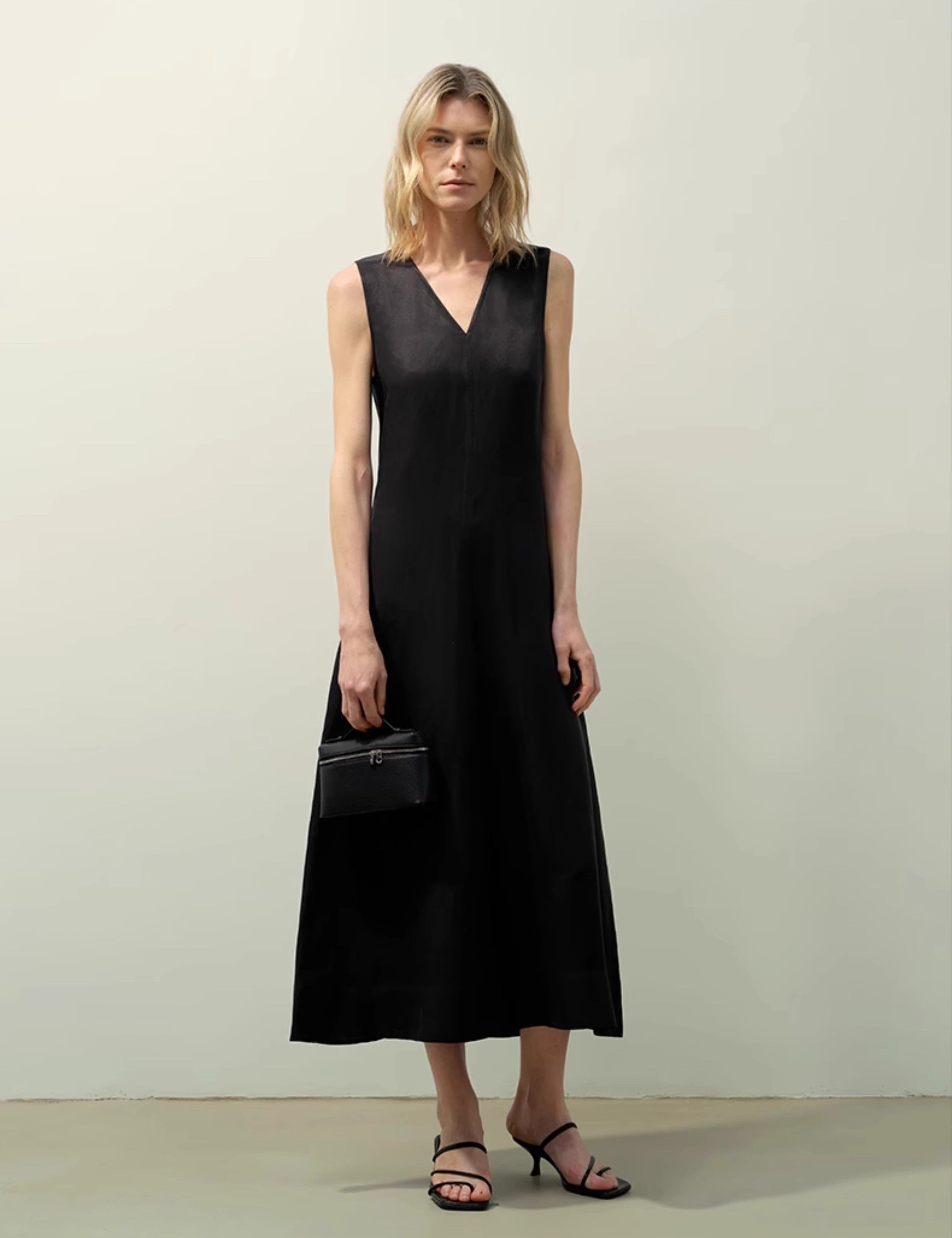 Woman wearing an Aurevae Cupro-Linen A-Line Dress in black, featuring a V-neck, sleeveless design, and mid-calf length with a smooth finish.