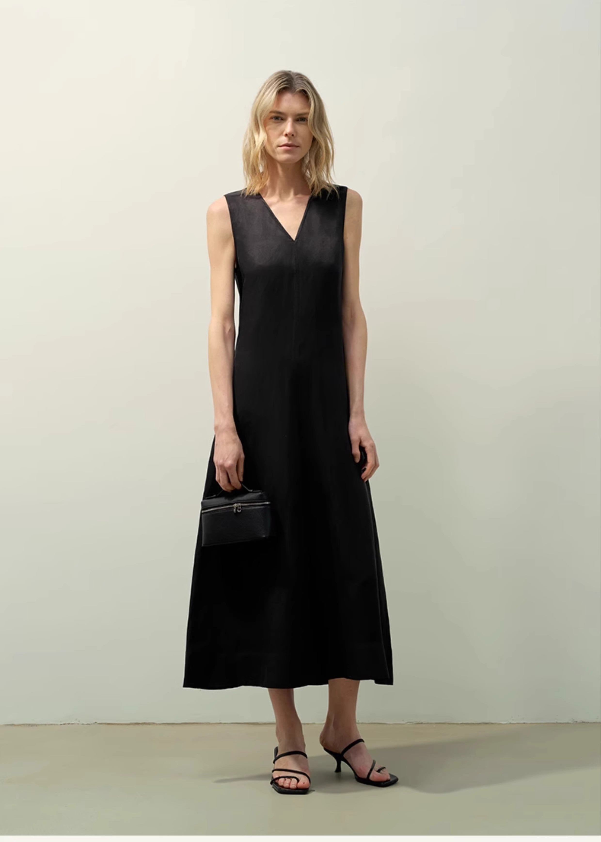 Woman wearing an Aurevae Cupro-Linen A-Line Dress in black, featuring a V-neck, sleeveless design, and mid-calf length with a smooth finish.