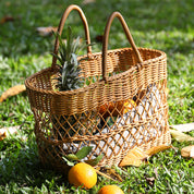 Handmade rattan-like picnic basket on grass, filled with fruits including a pineapple and oranges, ideal for outdoor outings and decor.