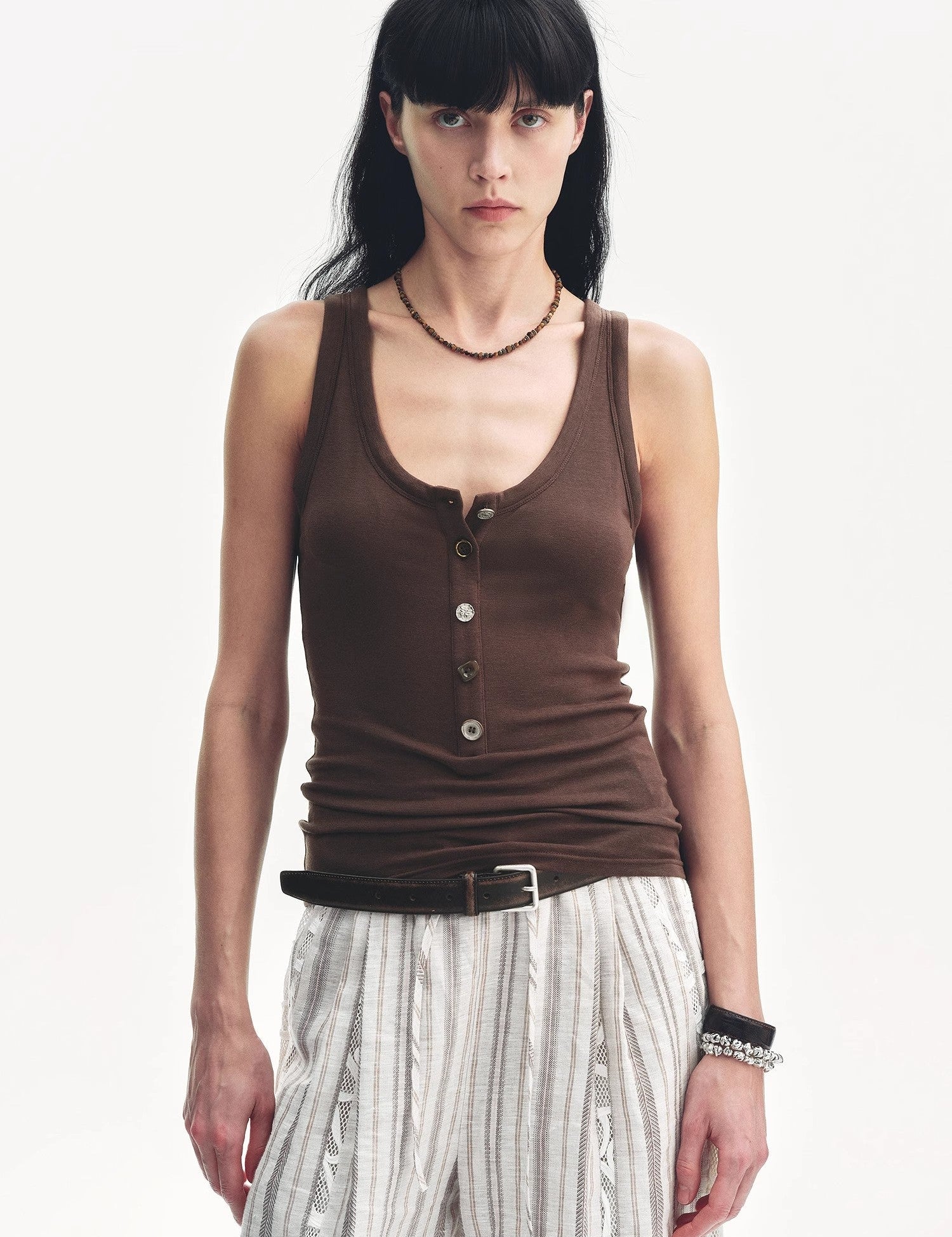 Woman wearing Lureva U-Henley Vest in brown, featuring a U-shaped neckline and wide straps, paired with striped pants.