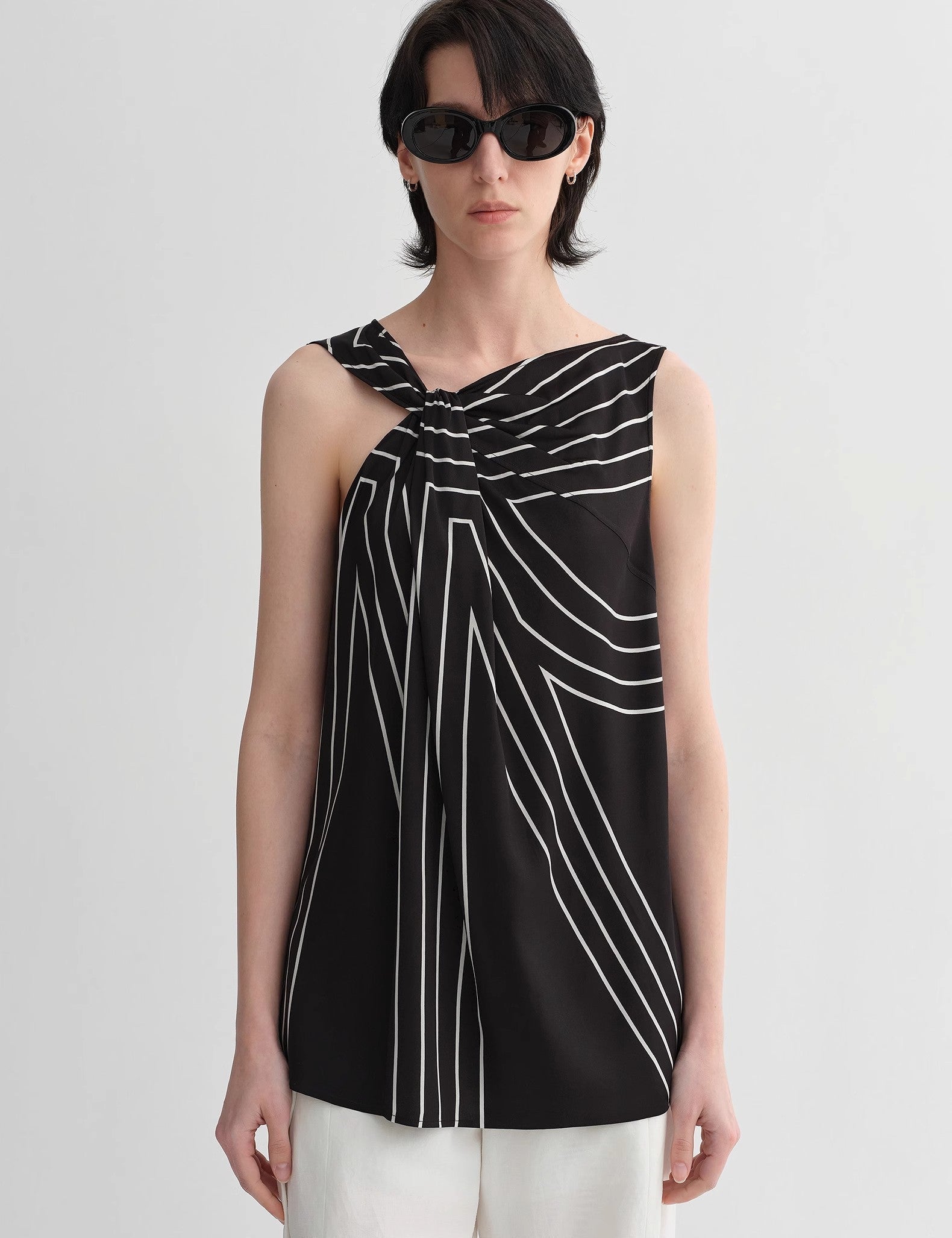 Seravelle Twisted Silk Vest with geometric print, sleeveless and asymmetrical, paired with white pants in a minimalist setting.