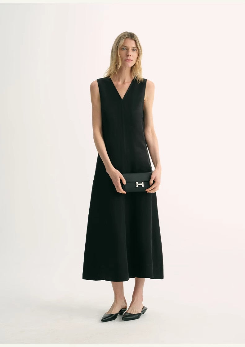 Model wearing black Aurevae Cupro-Linen A-Line Dress with V-neck and sleeveless design, paired with a clutch and flats.