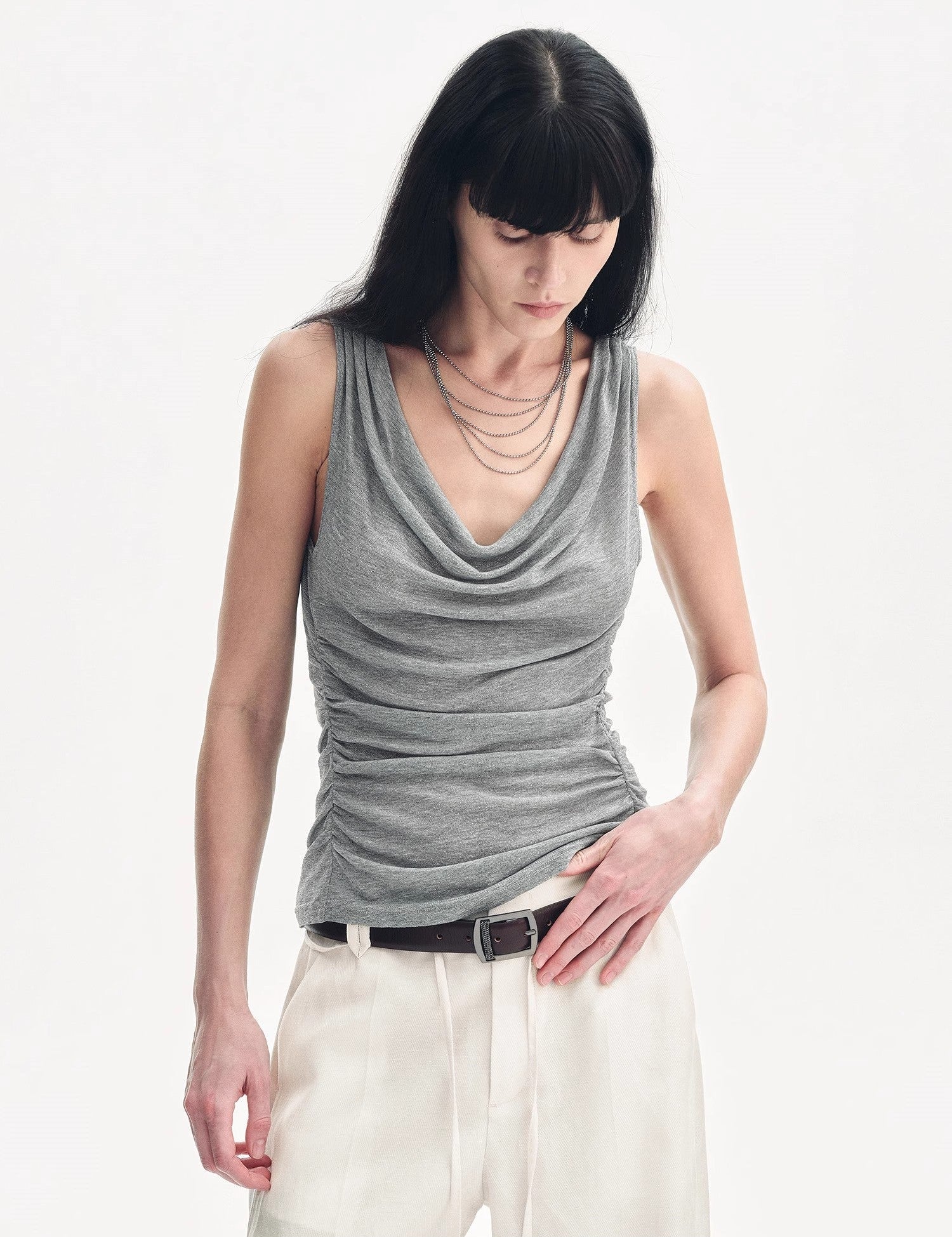 Woman wearing Zirellin Drape Contour Vest with pleated neckline and U-back, paired with white pants, showcasing feminine style.