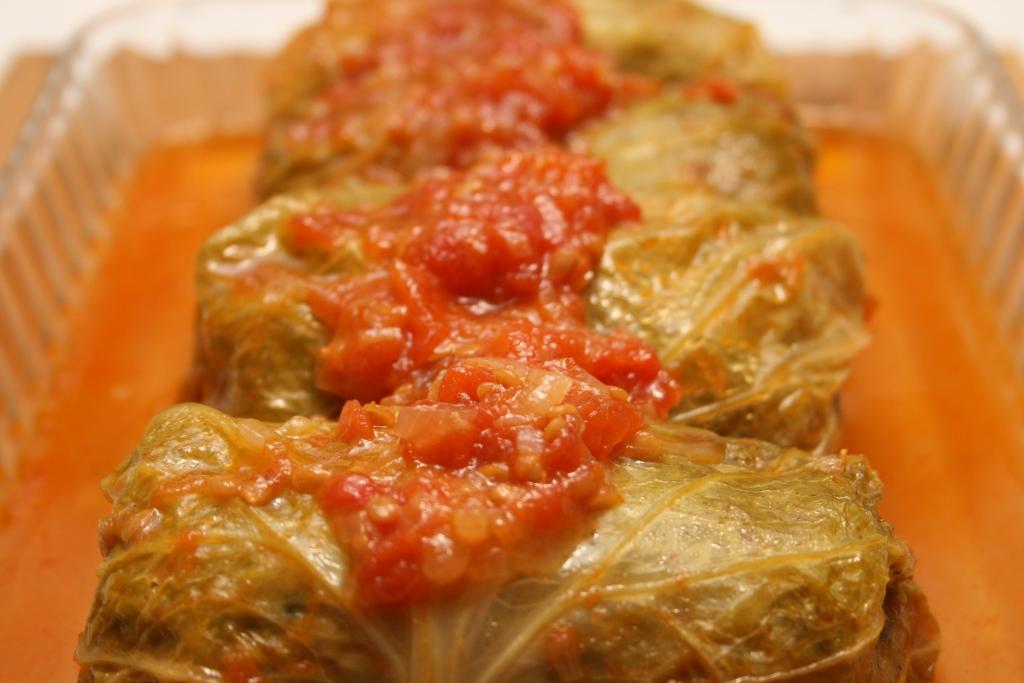 Homemade Ukrainian holubtsi stuffed cabbage rolls with savory filling, topped with tomato sauce, served in a clear dish.