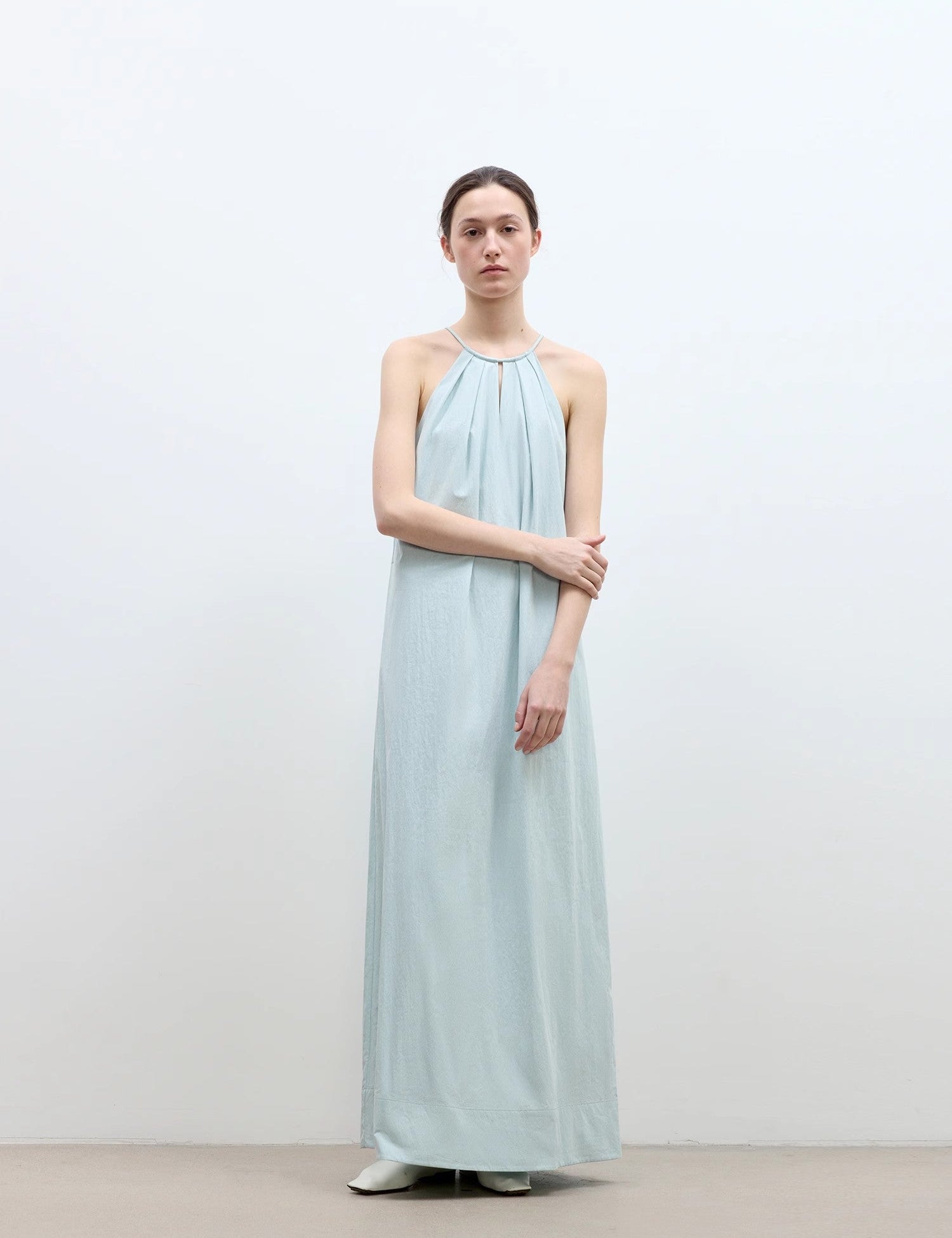 Woman wearing light blue Veridia Halter-Pleat Maxi Dress with cotton rope halter and fluid ankle-length skirt.