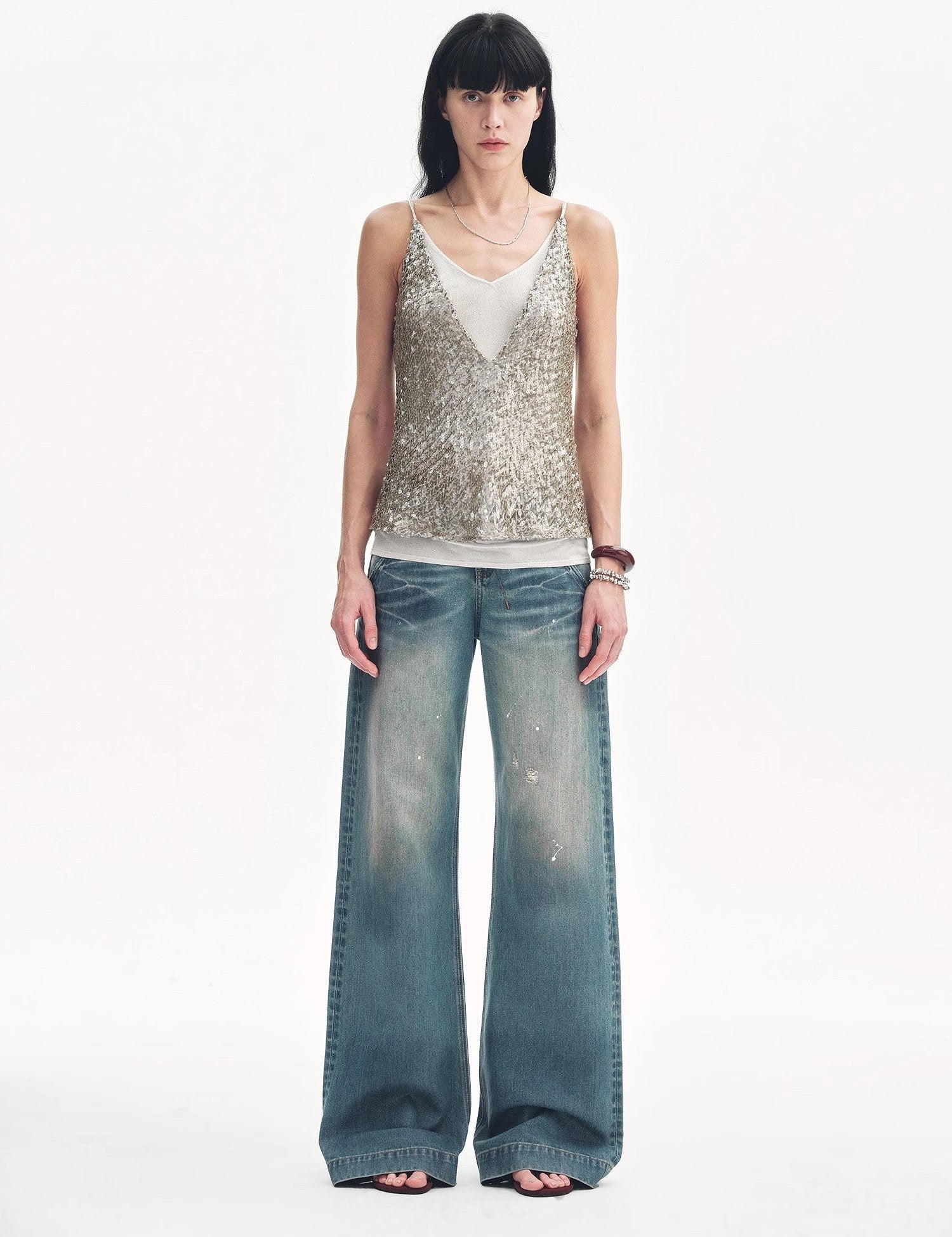 Woman wearing a silver sequin top and wide-leg jeans standing against a white background