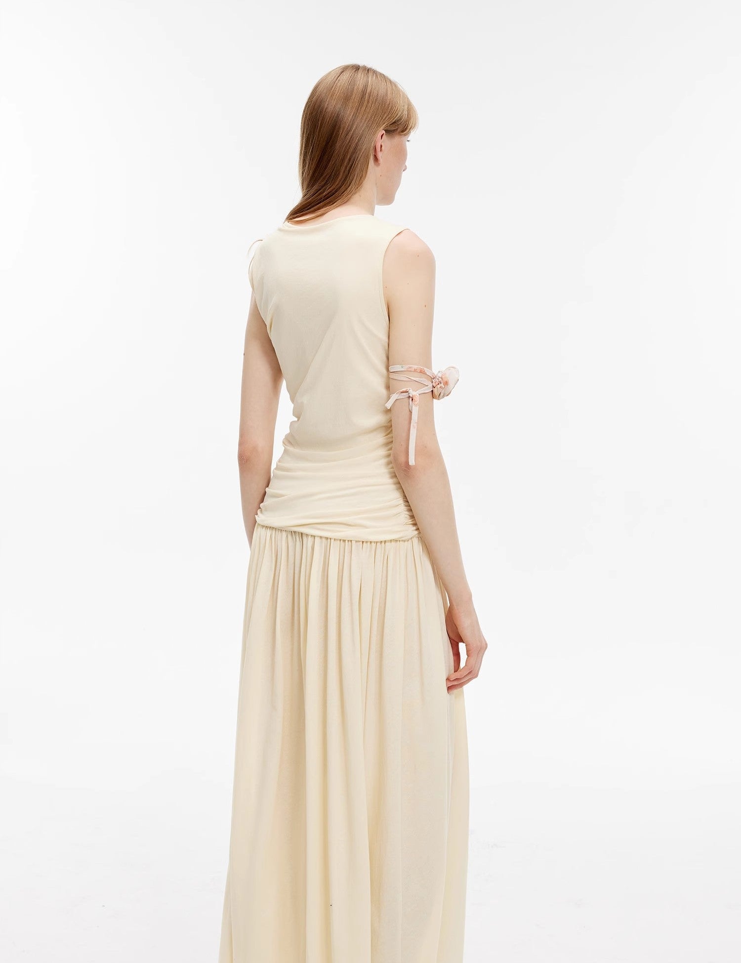 Back view of a model wearing an off-white pleated maxi dress showcasing its tailored fit and flowing design.