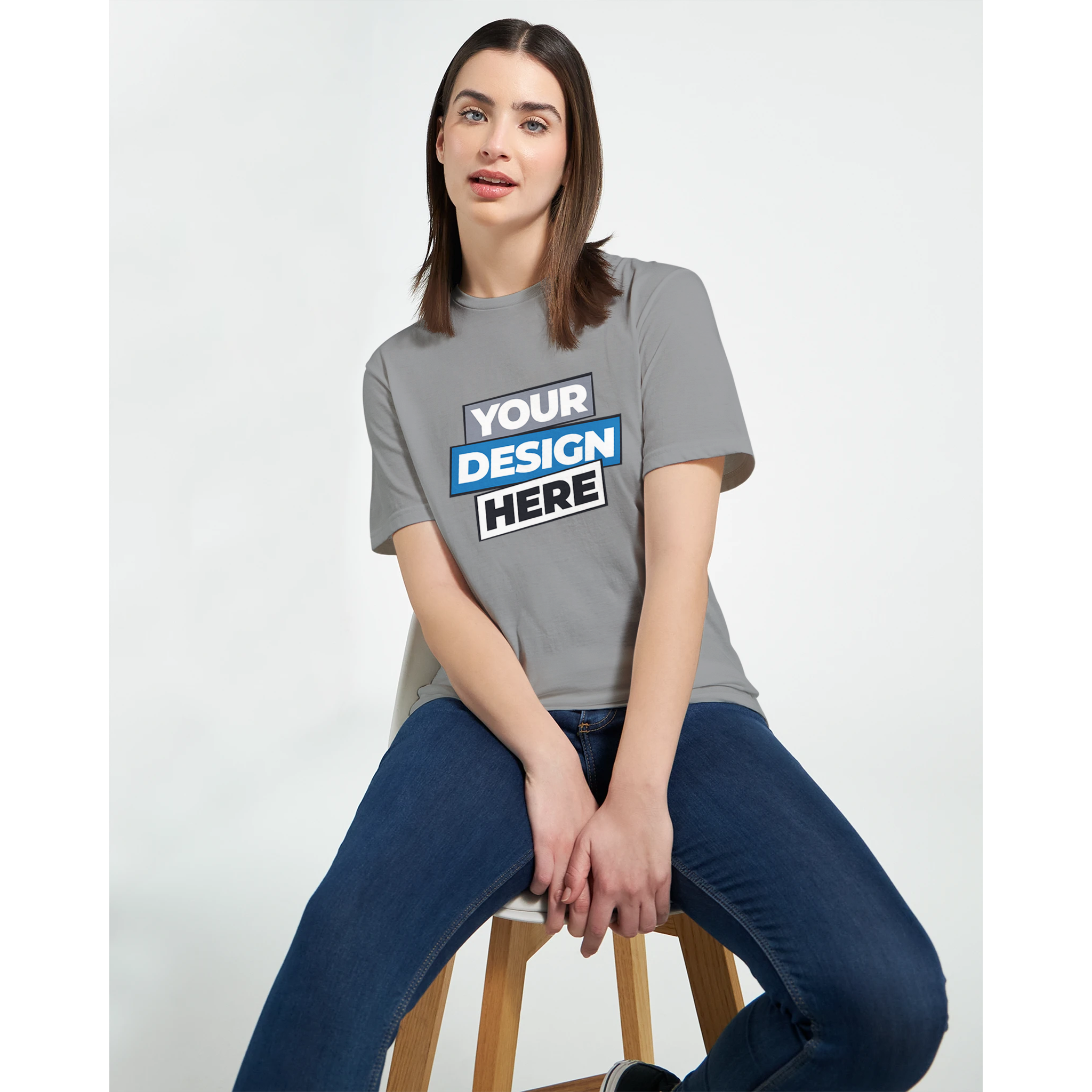Model wearing gray Zalmera women's cotton t-shirt with customizable print design, seated on a wooden stool against white background.