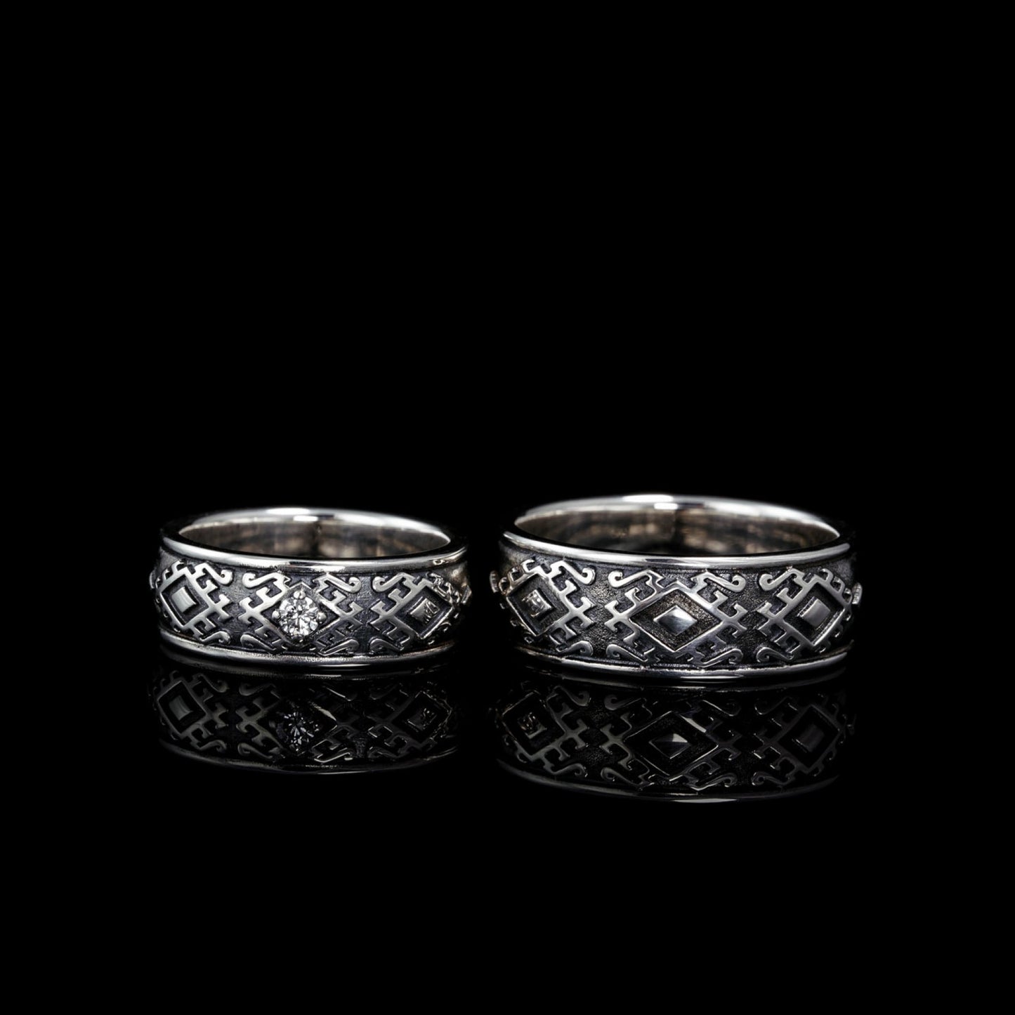 Sterling silver "Carpathian Harmony" wedding rings with oxidized finish and diamond, inspired by Hutsul heritage, on black background.