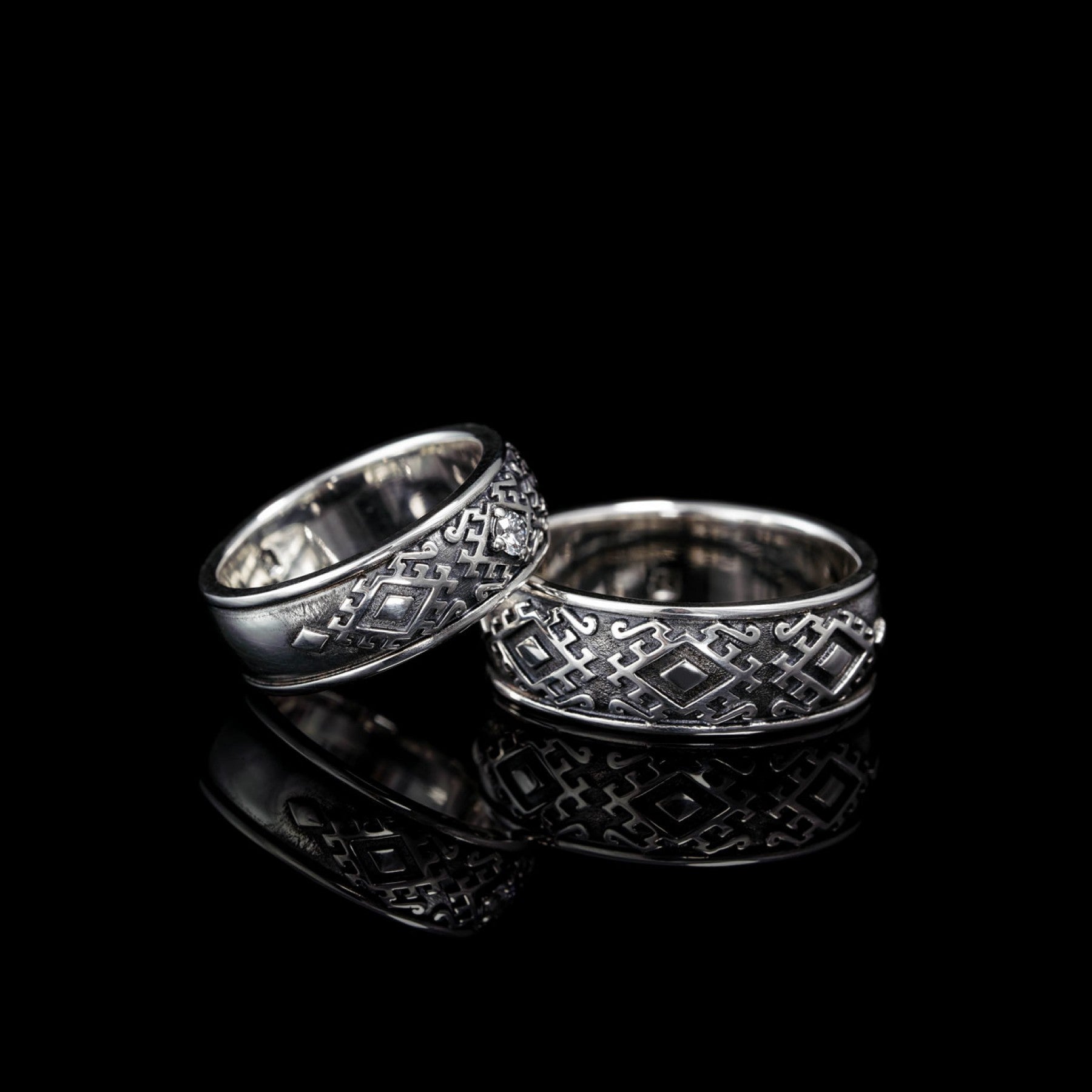 Sterling silver Carpathian Harmony wedding rings with oxidized finish, featuring intricate Hutsul design and natural diamond, on black background.