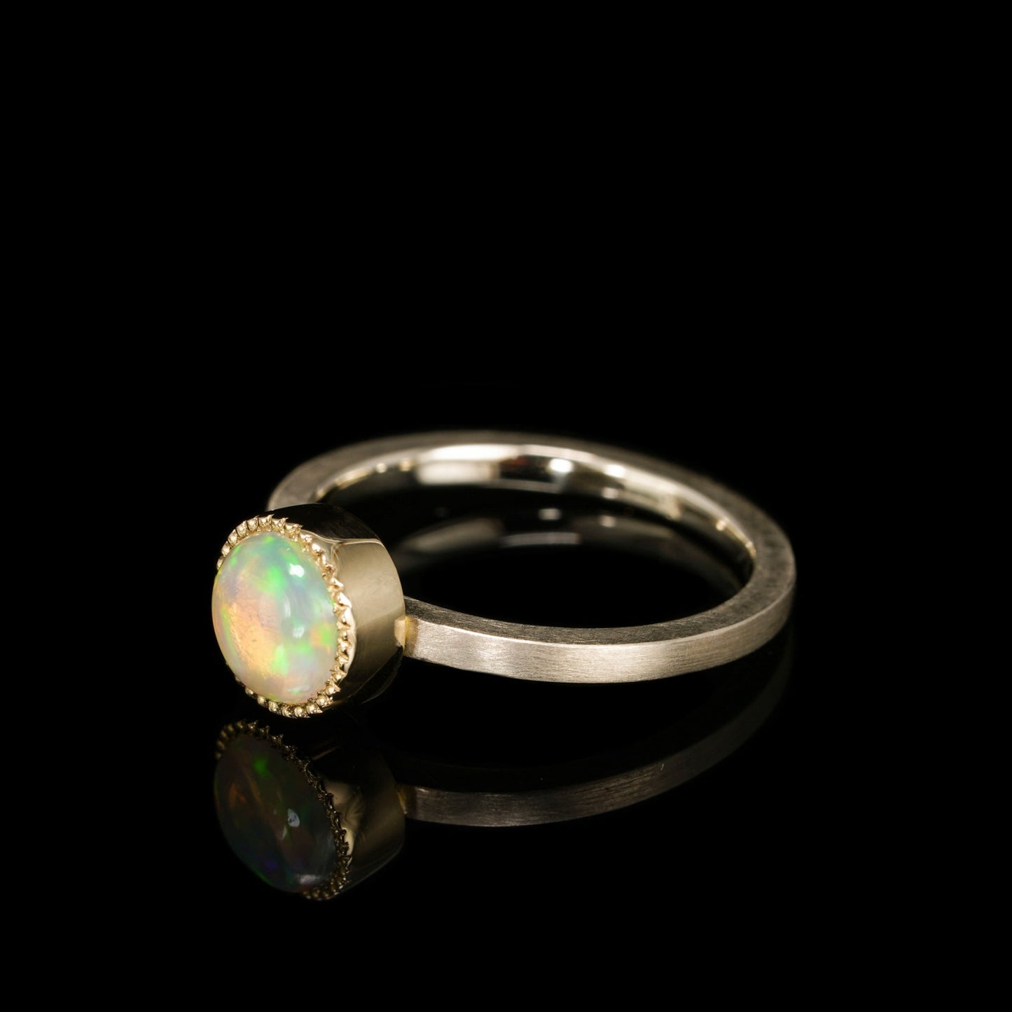 "Celestial Orbit ring with opal, crafted in white and 14K yellow gold, reflecting cosmic beauty against a black background."