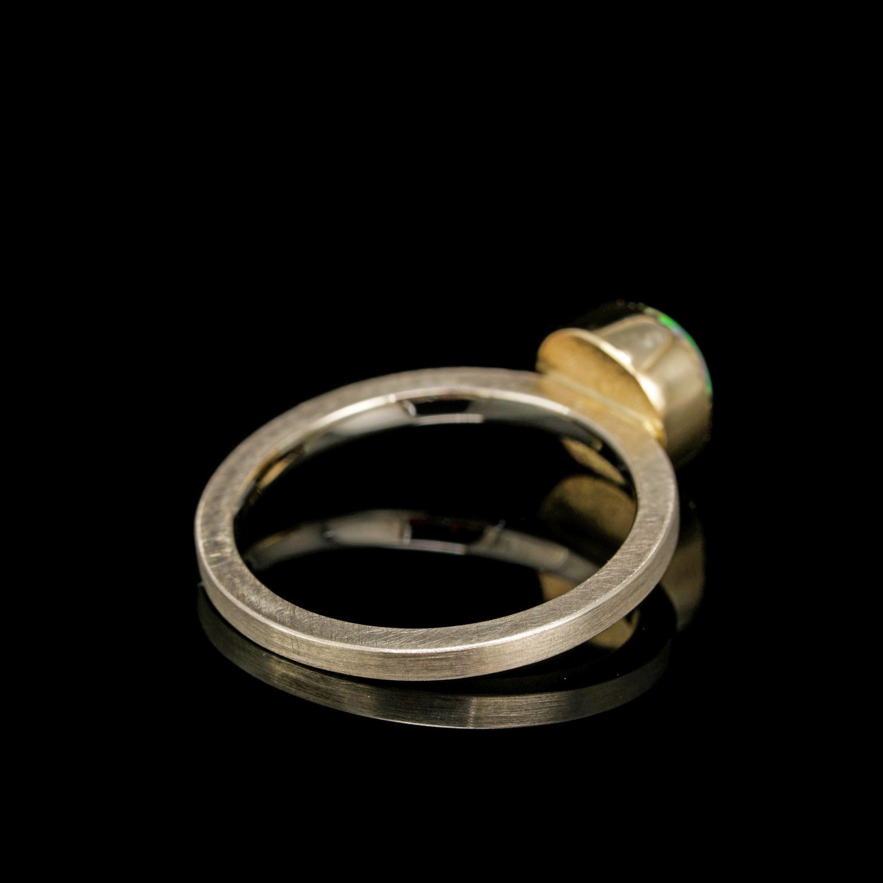 Celestial Orbit ring crafted from white and 14K yellow gold, featuring an opal stone, displayed on a reflective black background.