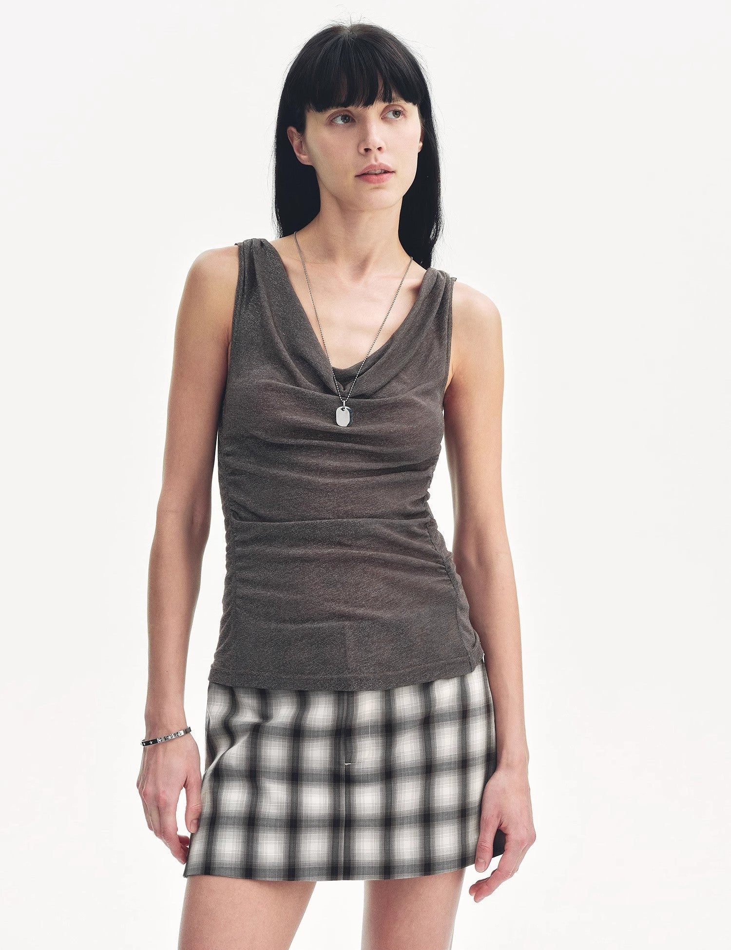 Zirellin Drape Contour Vest with sculptural pleats and adjustable drawstrings, worn with plaid skirt, showcasing modern femininity.