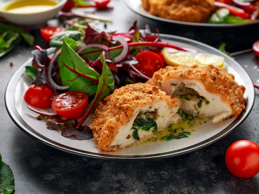 Homemade Kotleta Po-Kyivsky chicken cutlet with garlic butter, served with fresh salad and cherry tomatoes on a plate.